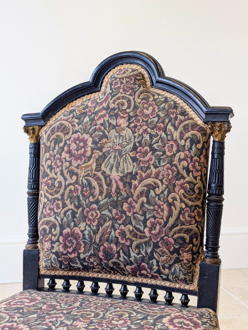 An antique Victorian ebonised low chair featuring a floral tapestry upholstered seat and backrest with turned spindle galleries and castors. View IV