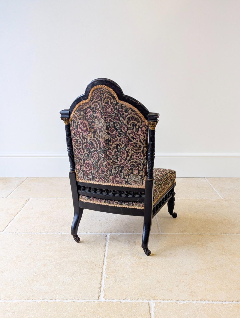 An antique Victorian ebonised low chair featuring a floral tapestry upholstered seat and backrest with turned spindle galleries and castors. View XII
