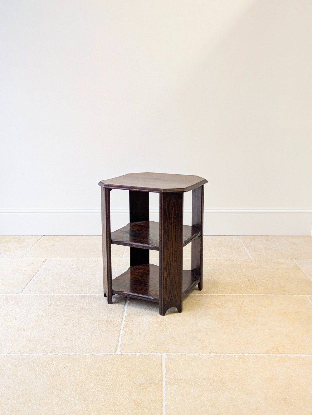 A dark brown oak book table with clipped corners on top and two open lower shelves supported by straight side legs.