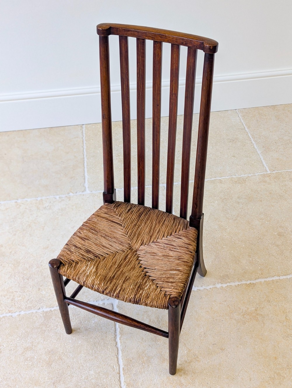An Arts and Crafts dark mahogany side chair featuring a tall vertical slat backrest, a woven rush seat, and simple turned legs with stretchers. View III