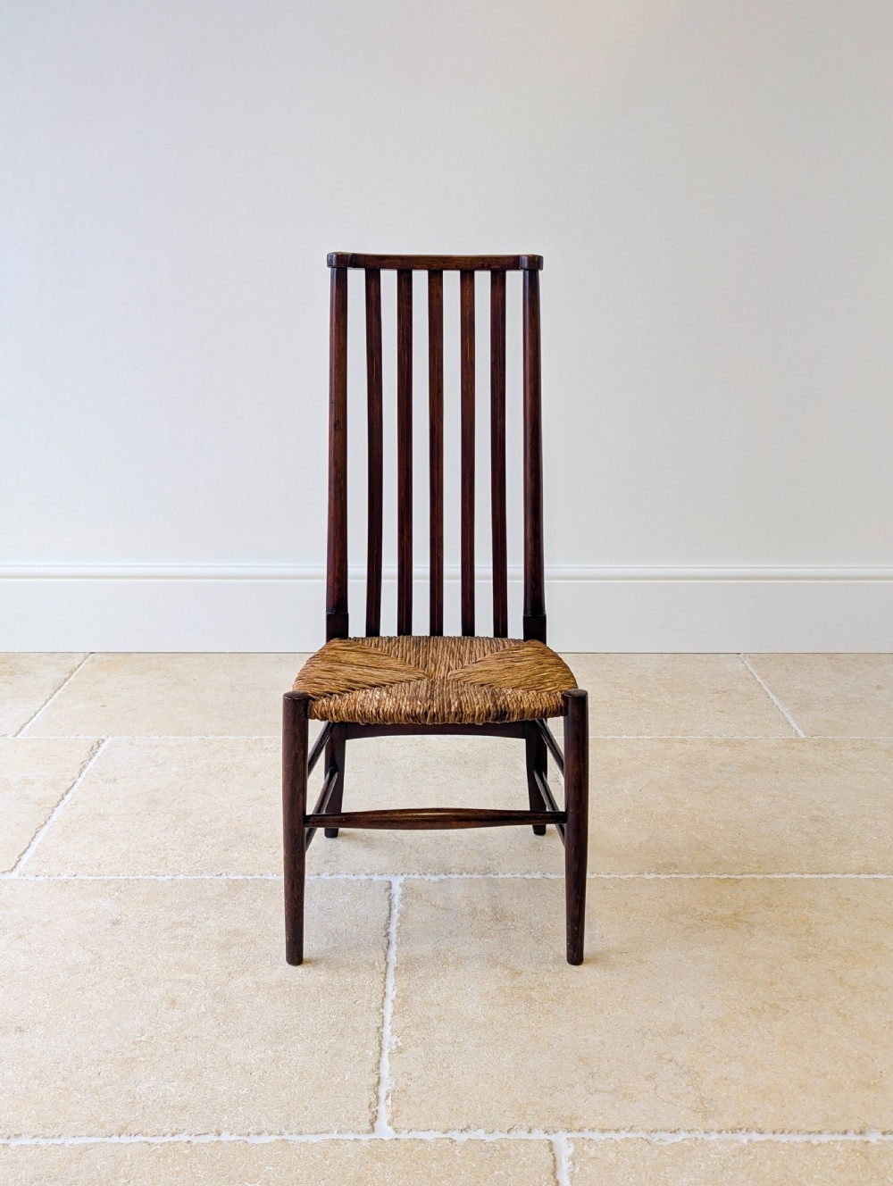 An Arts and Crafts dark mahogany side chair featuring a tall vertical slat backrest, a woven rush seat, and simple turned legs with stretchers. View V