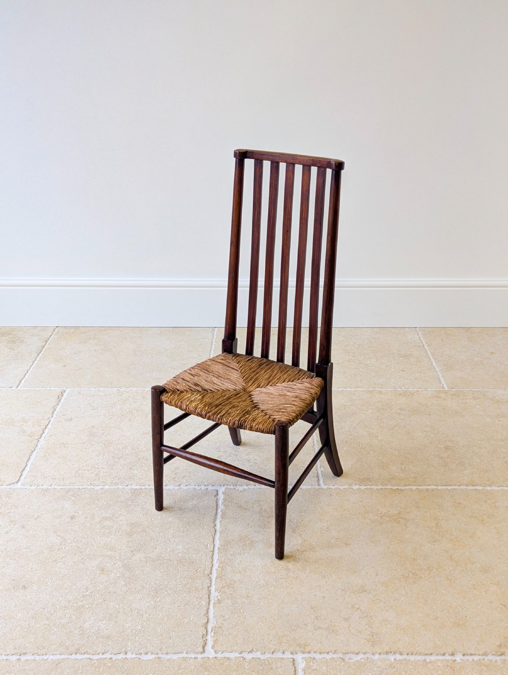 An Arts and Crafts dark mahogany side chair featuring a tall vertical slat backrest, a woven rush seat, and simple turned legs with stretchers. View VI
