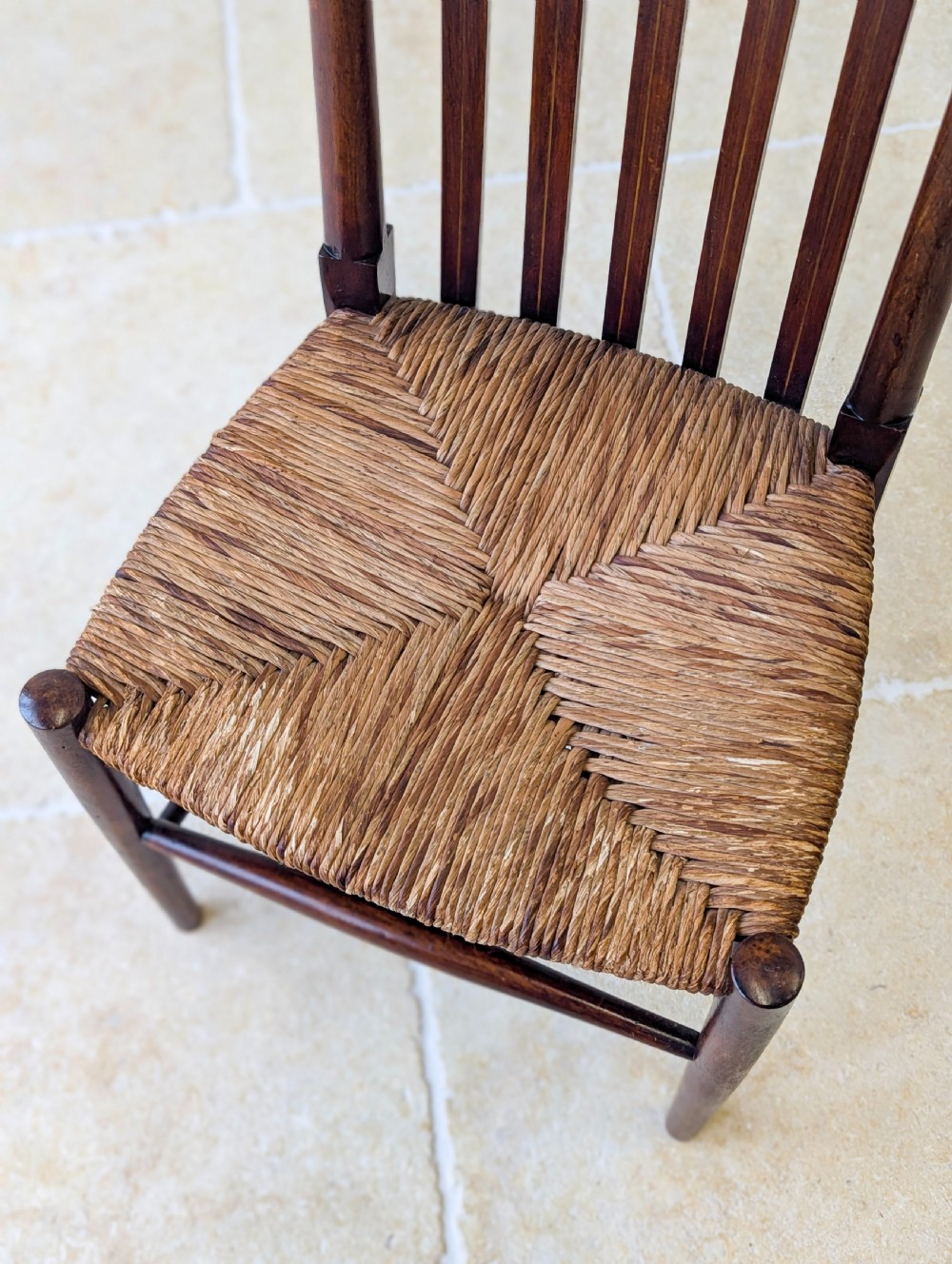 An Arts and Crafts dark mahogany side chair featuring a tall vertical slat backrest, a woven rush seat, and simple turned legs with stretchers. View VII