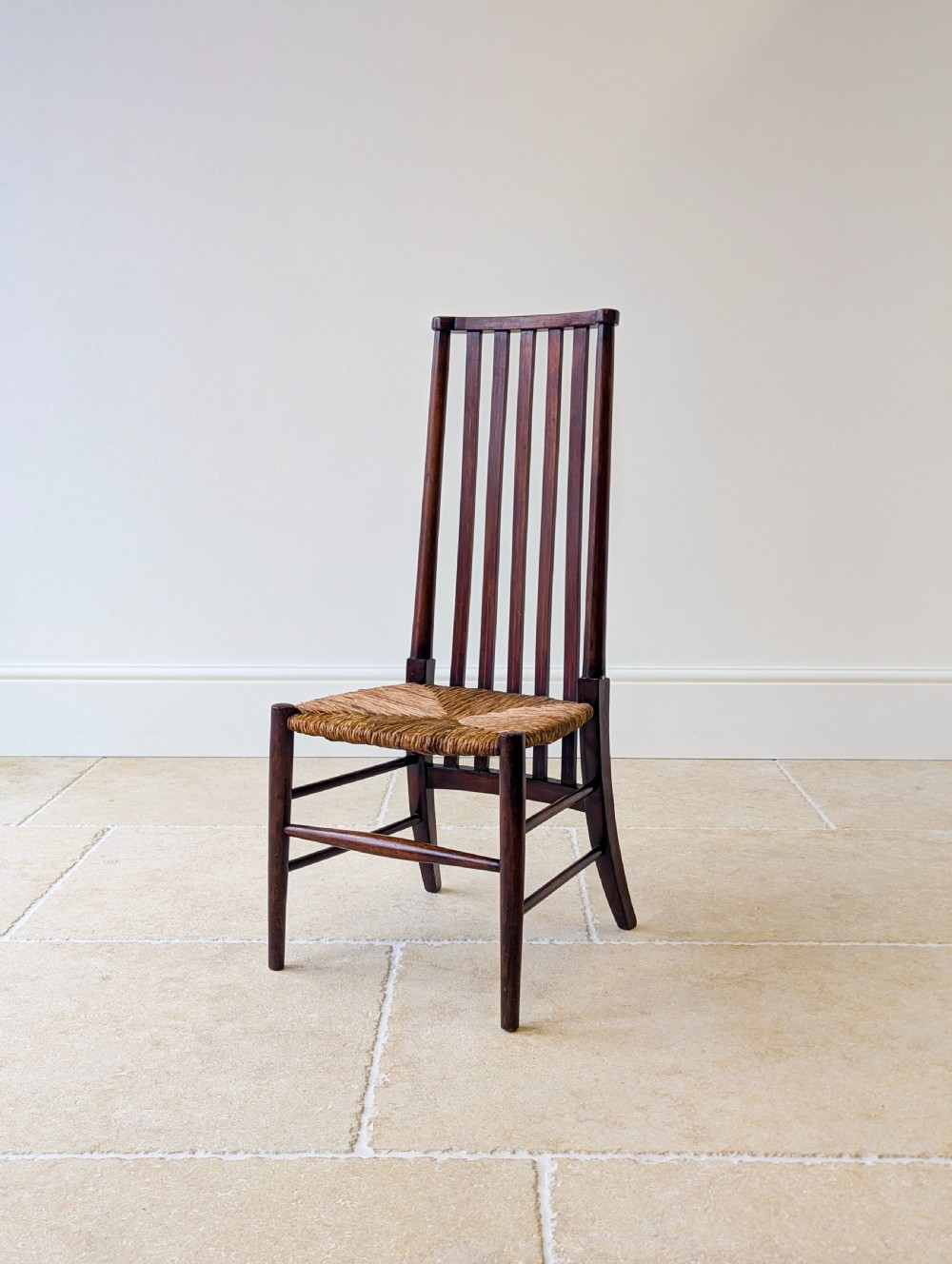 An Arts and Crafts dark mahogany side chair featuring a tall vertical slat backrest, a woven rush seat, and simple turned legs with stretchers. View X