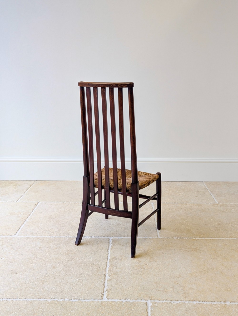 An Arts and Crafts dark mahogany side chair featuring a tall vertical slat backrest, a woven rush seat, and simple turned legs with stretchers. View XV