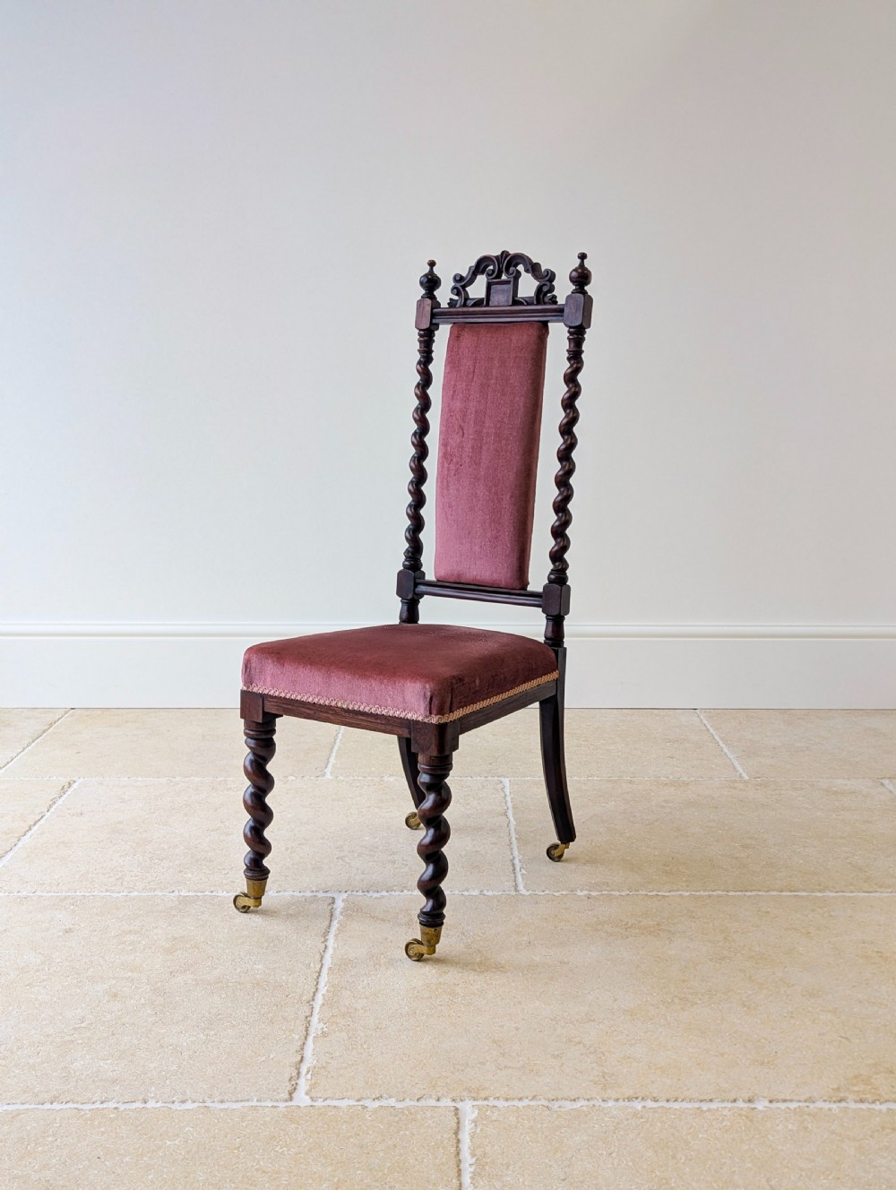 A Victorian rosewood side chair featuring barley twist legs and uprights, a carved cresting rail, dusty pink velvet upholstery, and brass castors.