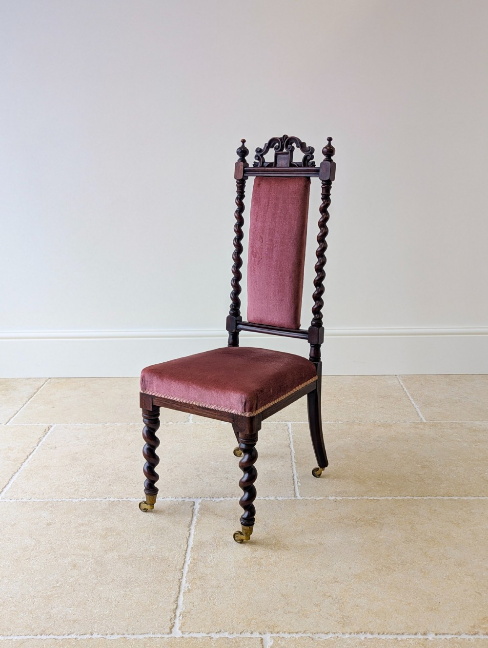 A Victorian rosewood side chair featuring barley twist legs and uprights, a carved cresting rail, dusty pink velvet upholstery, and brass castors. View V
