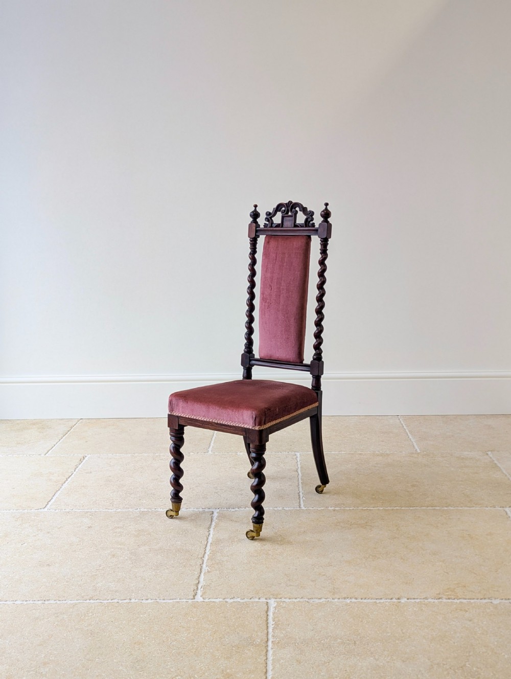 A Victorian rosewood side chair featuring barley twist legs and uprights, a carved cresting rail, dusty pink velvet upholstery, and brass castors. View VII