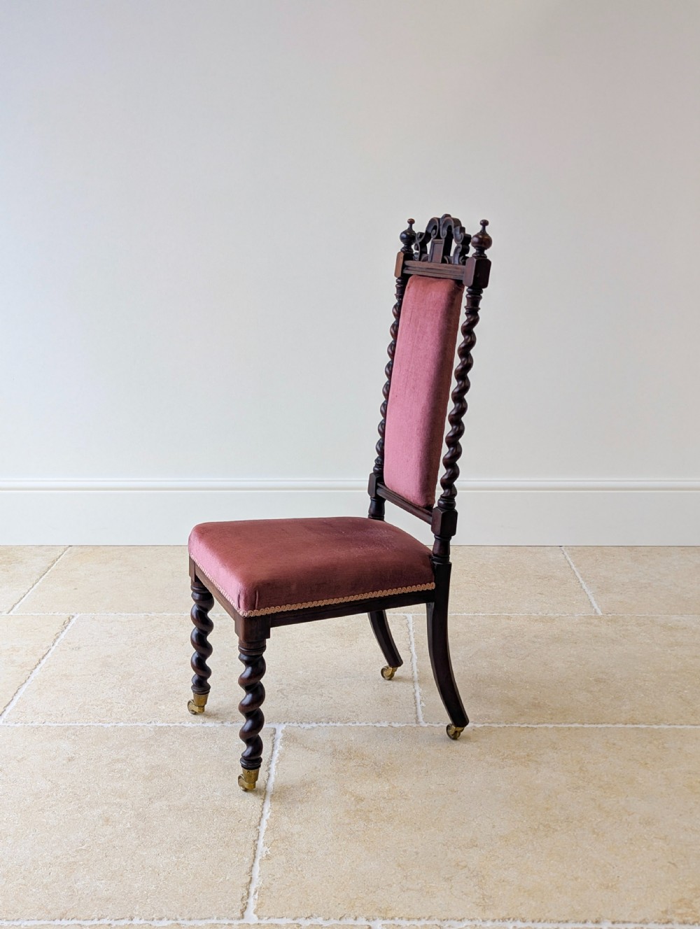 A Victorian rosewood side chair featuring barley twist legs and uprights, a carved cresting rail, dusty pink velvet upholstery, and brass castors. View XI