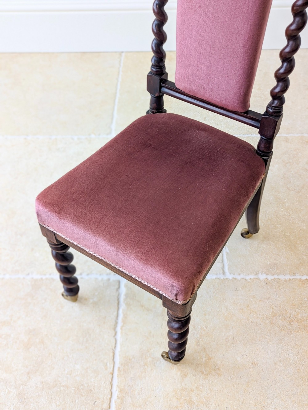 A Victorian rosewood side chair featuring barley twist legs and uprights, a carved cresting rail, dusty pink velvet upholstery, and brass castors. View XII