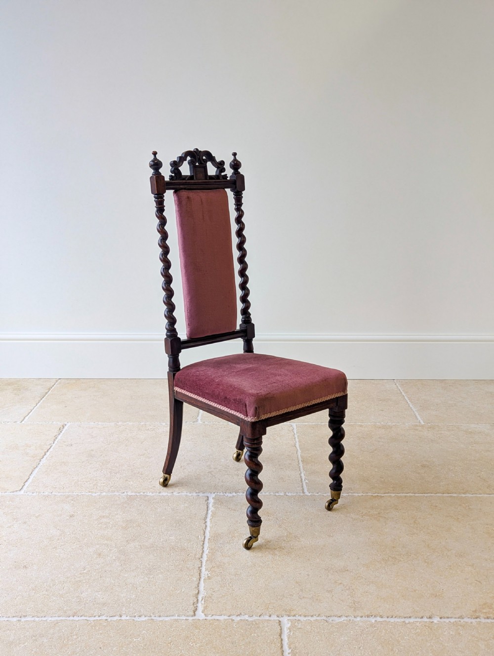 A Victorian rosewood side chair featuring barley twist legs and uprights, a carved cresting rail, dusty pink velvet upholstery, and brass castors. View XIII