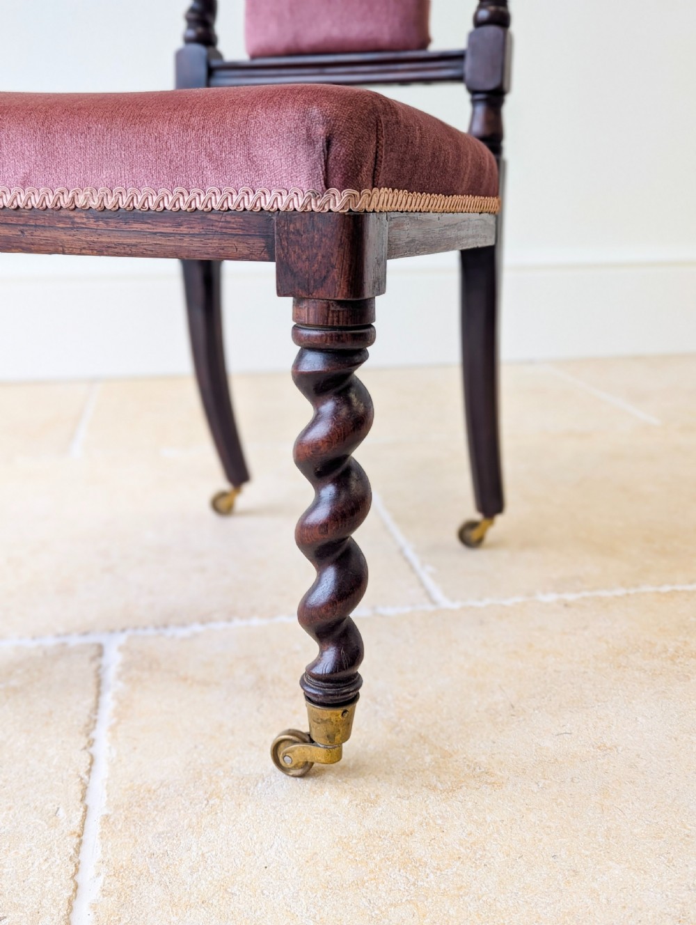 A Victorian rosewood side chair featuring barley twist legs and uprights, a carved cresting rail, dusty pink velvet upholstery, and brass castors. View XIV