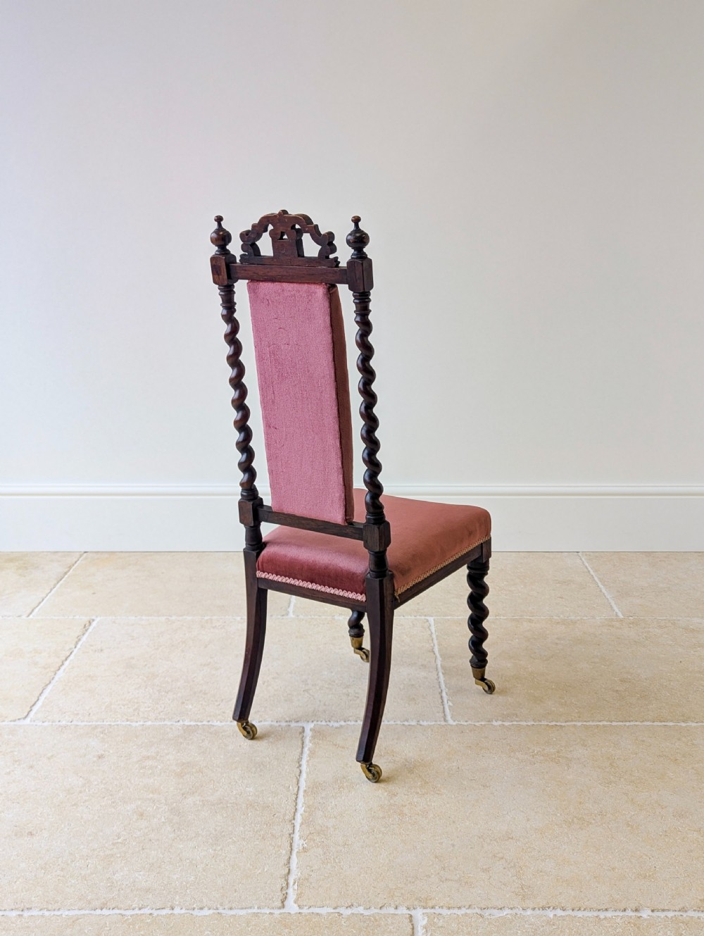 A Victorian rosewood side chair featuring barley twist legs and uprights, a carved cresting rail, dusty pink velvet upholstery, and brass castors. View XVI