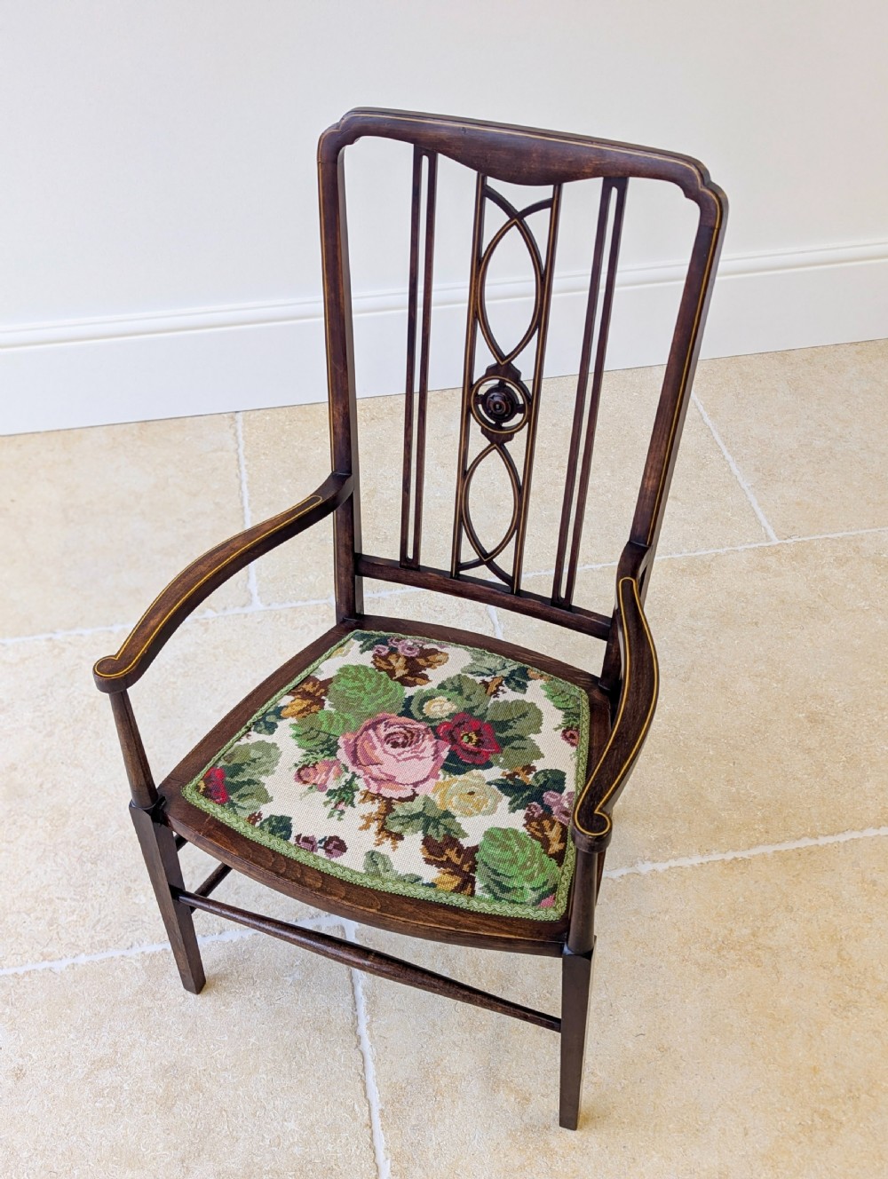 An Edwardian dark mahogany elbow chair featuring a tall pierced splat back, sloped armrests, straight legs with stretchers, and a floral tapestry seat. View II