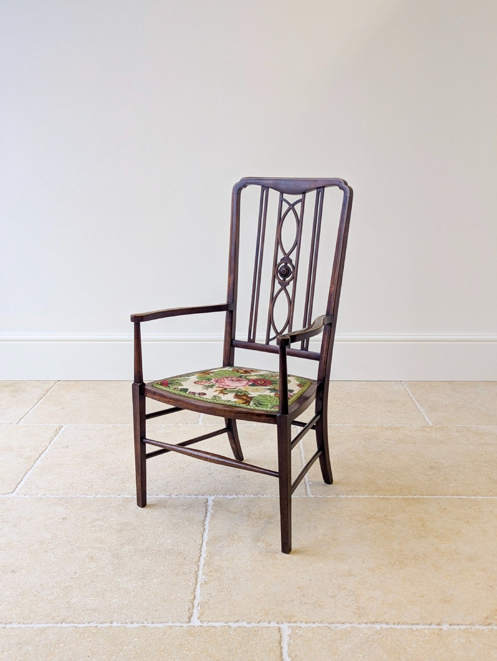 An Edwardian dark mahogany elbow chair featuring a tall pierced splat back, sloped armrests, straight legs with stretchers, and a floral tapestry seat. View III