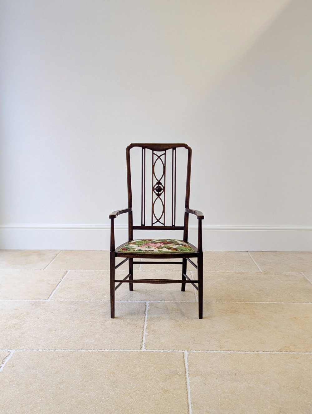 An Edwardian dark mahogany elbow chair featuring a tall pierced splat back, sloped armrests, straight legs with stretchers, and a floral tapestry seat. View V