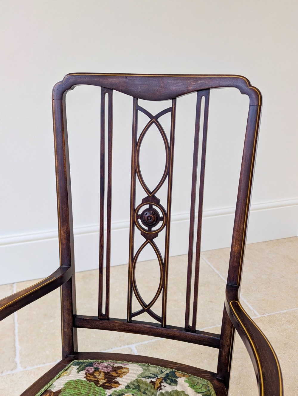 An Edwardian dark mahogany elbow chair featuring a tall pierced splat back, sloped armrests, straight legs with stretchers, and a floral tapestry seat. View VI