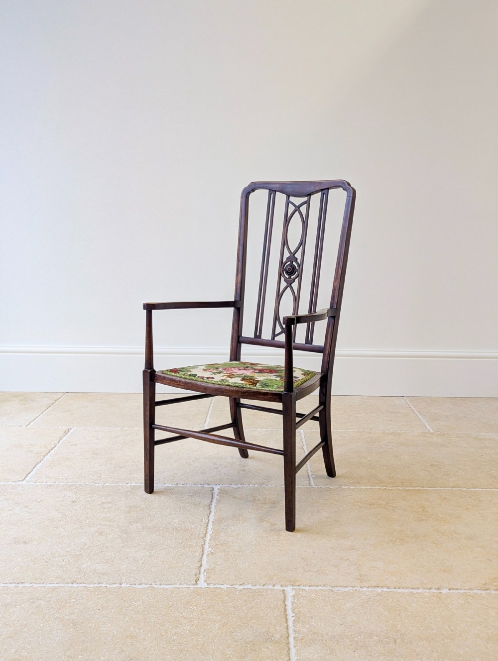 An Edwardian dark mahogany elbow chair featuring a tall pierced splat back, sloped armrests, straight legs with stretchers, and a floral tapestry seat. View VII