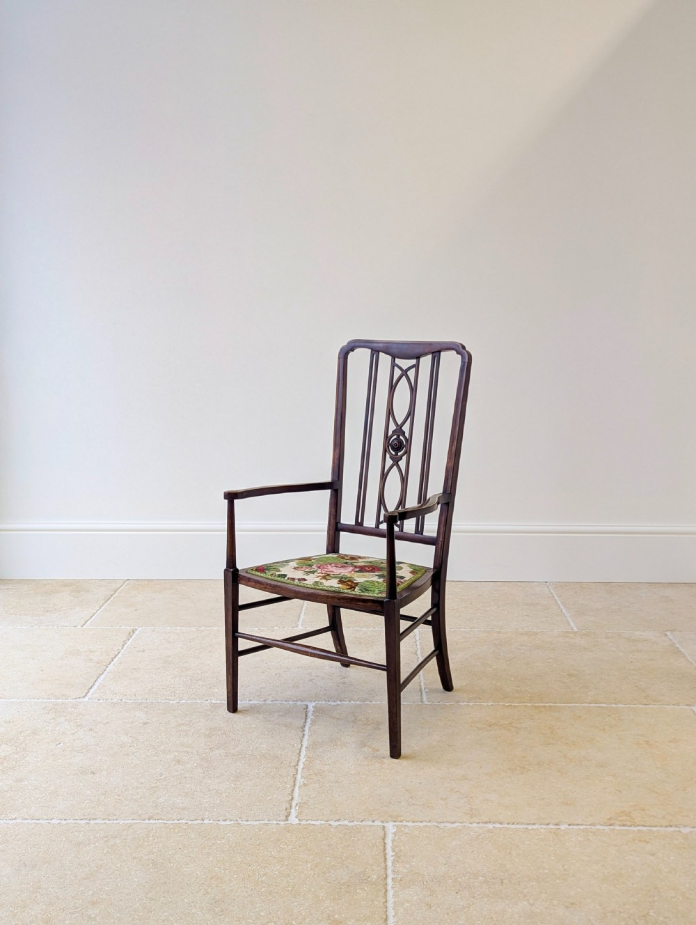 An Edwardian dark mahogany elbow chair featuring a tall pierced splat back, sloped armrests, straight legs with stretchers, and a floral tapestry seat. View IX