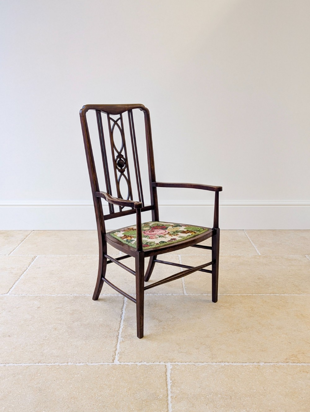 An Edwardian dark mahogany elbow chair featuring a tall pierced splat back, sloped armrests, straight legs with stretchers, and a floral tapestry seat. View XIII