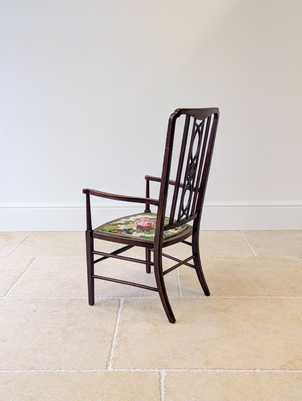 An Edwardian dark mahogany elbow chair featuring a tall pierced splat back, sloped armrests, straight legs with stretchers, and a floral tapestry seat. View XV
