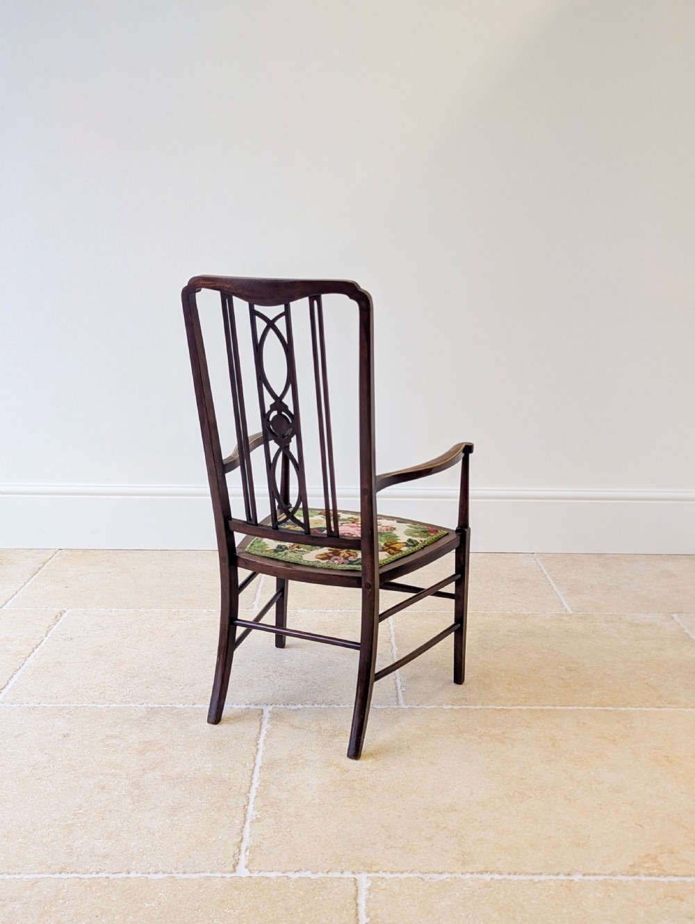 An Edwardian dark mahogany elbow chair featuring a tall pierced splat back, sloped armrests, straight legs with stretchers, and a floral tapestry seat. View XVI