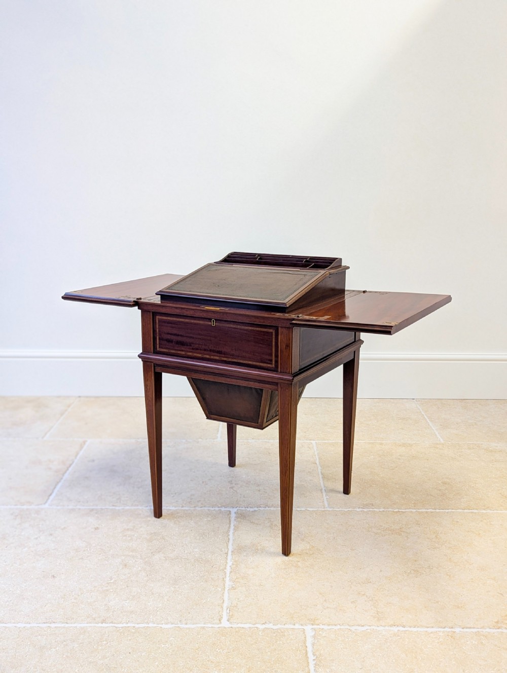 An Edwardian dark mahogany metamorphic writing table featuring two hinged side flaps, a sloped leather writing surface, integrated stationery dividers, and tapered legs.