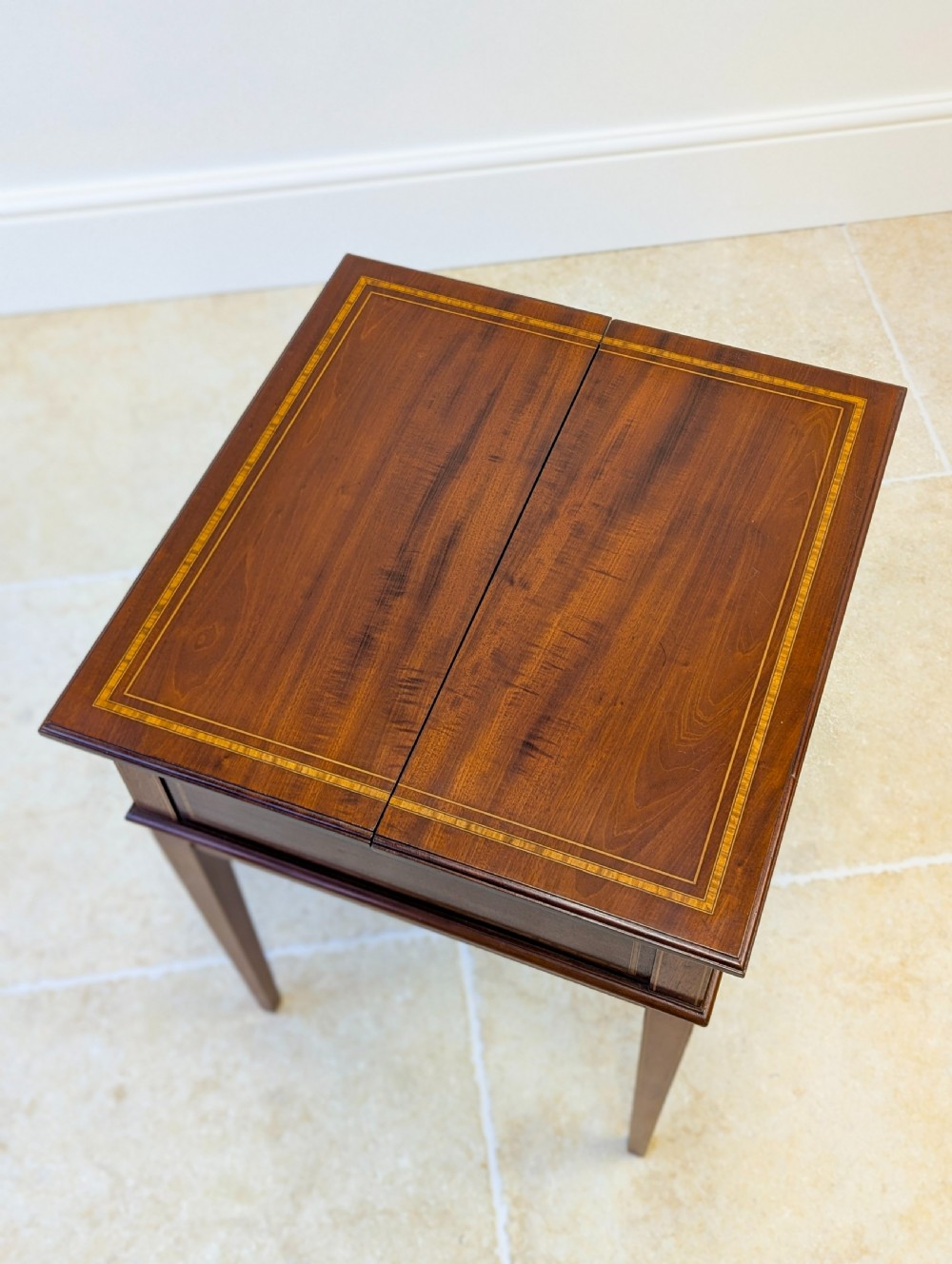 An Edwardian dark mahogany metamorphic writing table featuring two hinged side flaps, a sloped leather writing surface, integrated stationery dividers, and tapered legs. View III