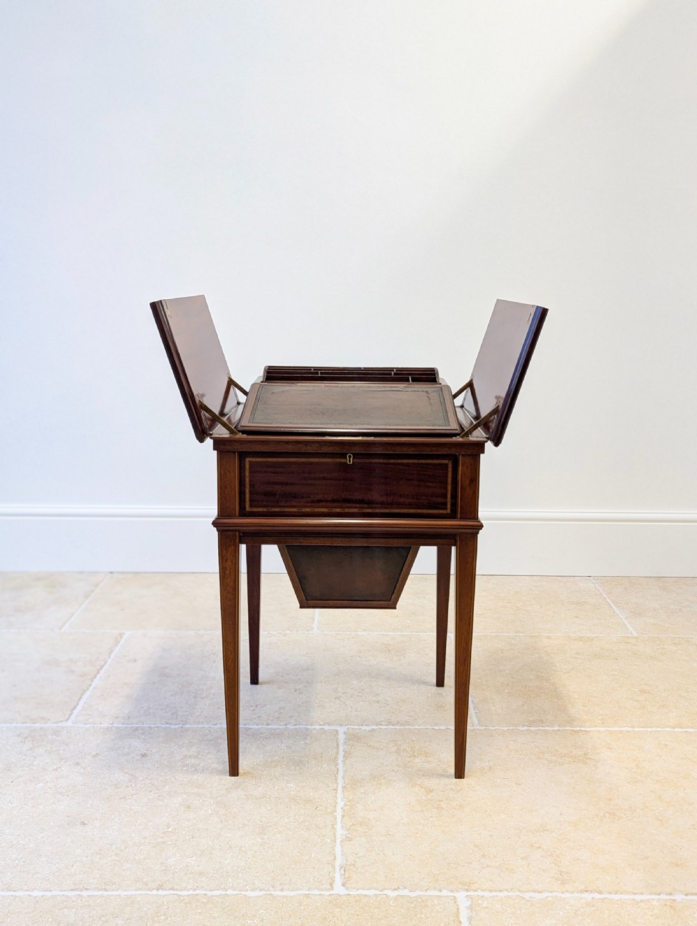 An Edwardian dark mahogany metamorphic writing table featuring two hinged side flaps, a sloped leather writing surface, integrated stationery dividers, and tapered legs. View IV