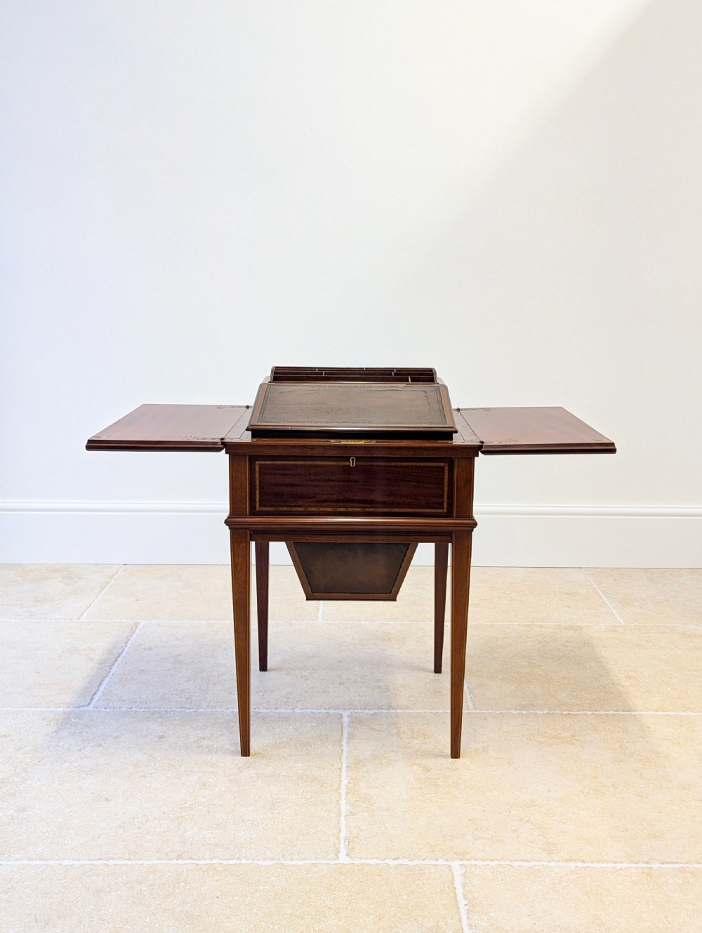 An Edwardian dark mahogany metamorphic writing table featuring two hinged side flaps, a sloped leather writing surface, integrated stationery dividers, and tapered legs. View V