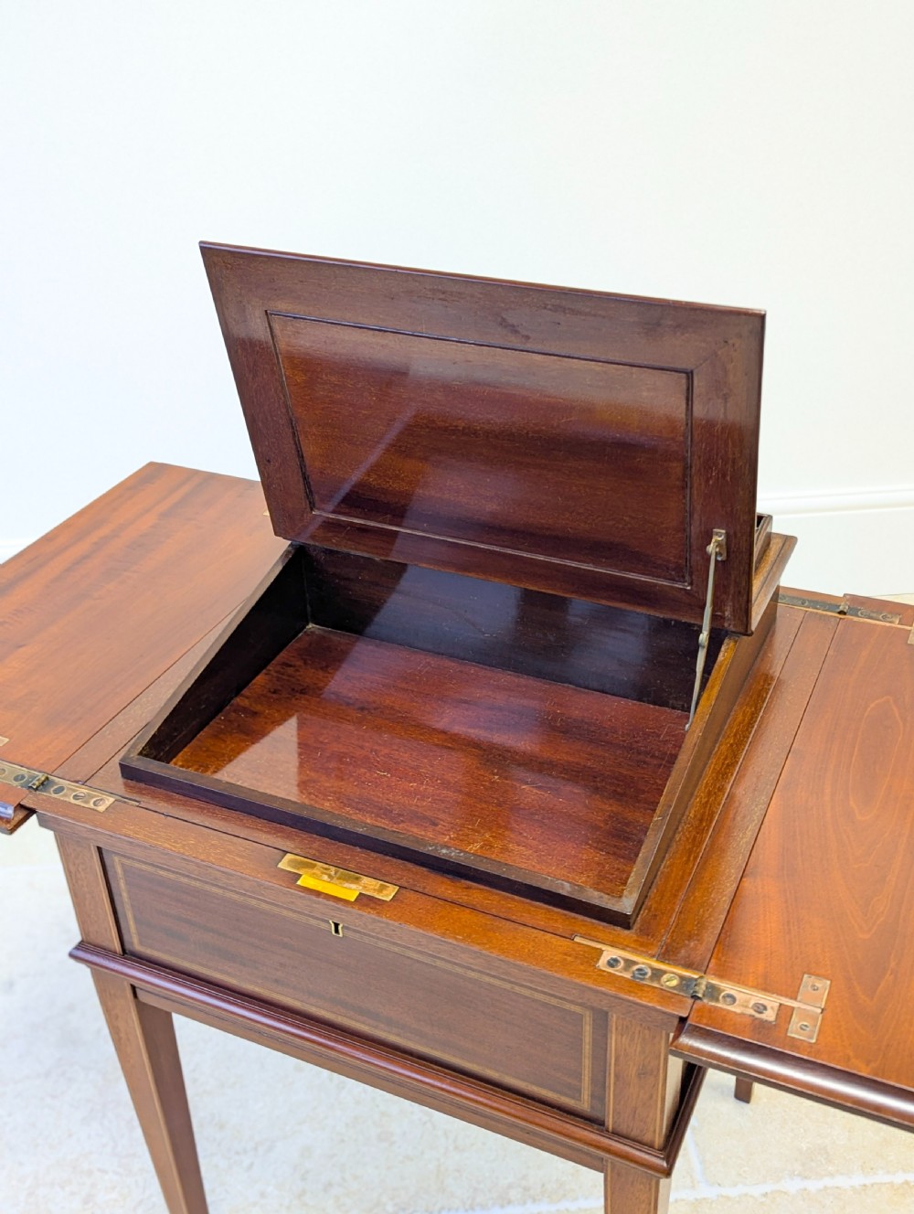 An Edwardian dark mahogany metamorphic writing table featuring two hinged side flaps, a sloped leather writing surface, integrated stationery dividers, and tapered legs. View VII