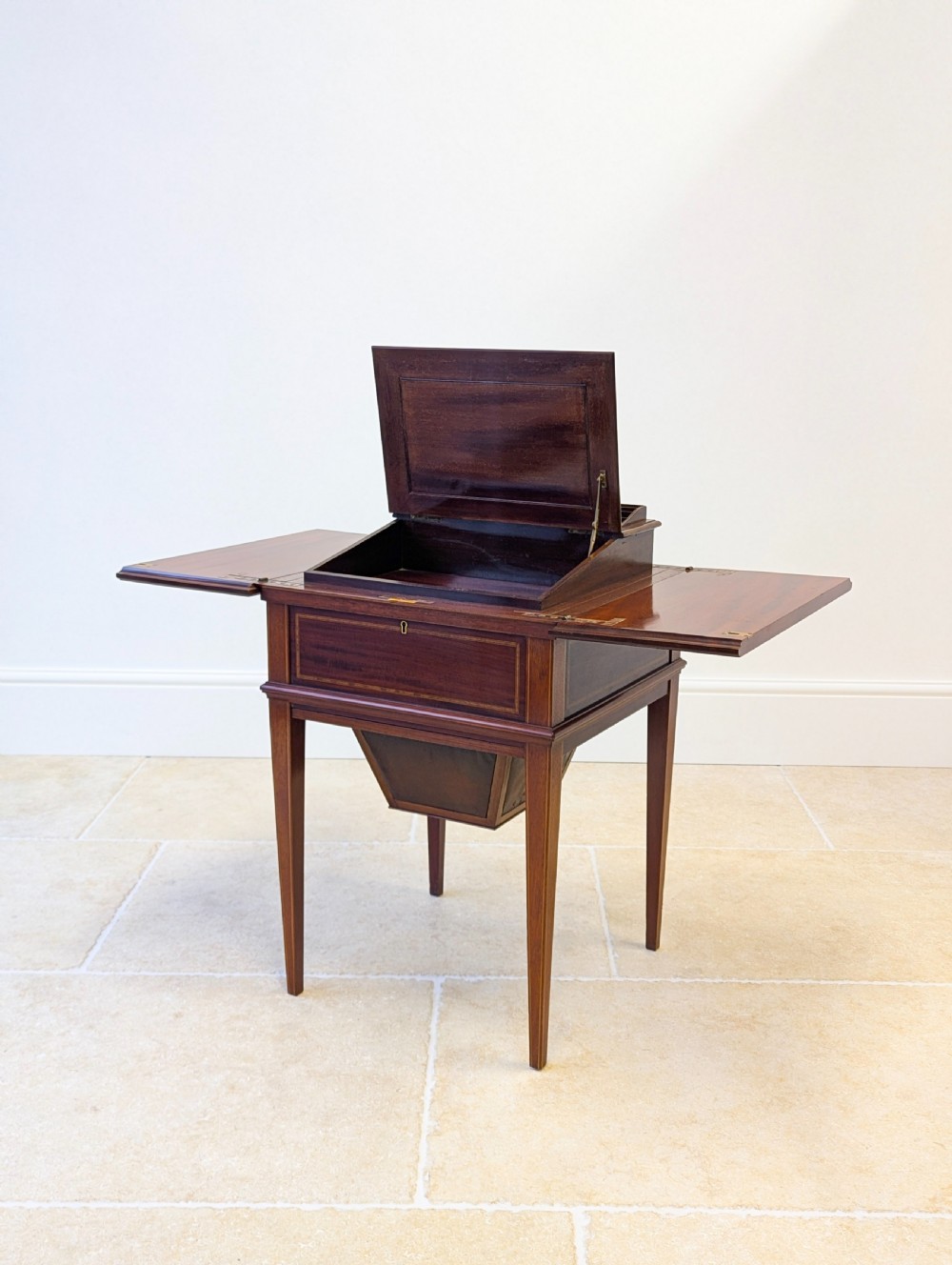 An Edwardian dark mahogany metamorphic writing table featuring two hinged side flaps, a sloped leather writing surface, integrated stationery dividers, and tapered legs. View VIII