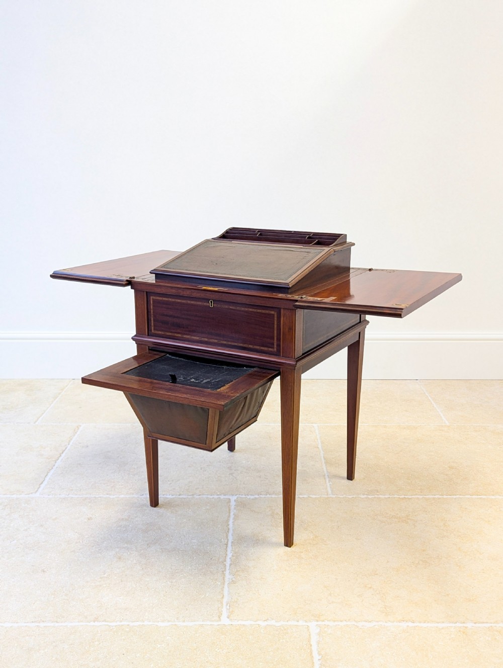 An Edwardian dark mahogany metamorphic writing table featuring two hinged side flaps, a sloped leather writing surface, integrated stationery dividers, and tapered legs. View IX
