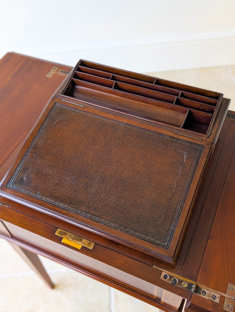 An Edwardian dark mahogany metamorphic writing table featuring two hinged side flaps, a sloped leather writing surface, integrated stationery dividers, and tapered legs. View X