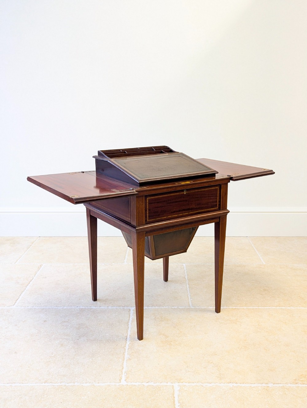 An Edwardian dark mahogany metamorphic writing table featuring two hinged side flaps, a sloped leather writing surface, integrated stationery dividers, and tapered legs. View XII