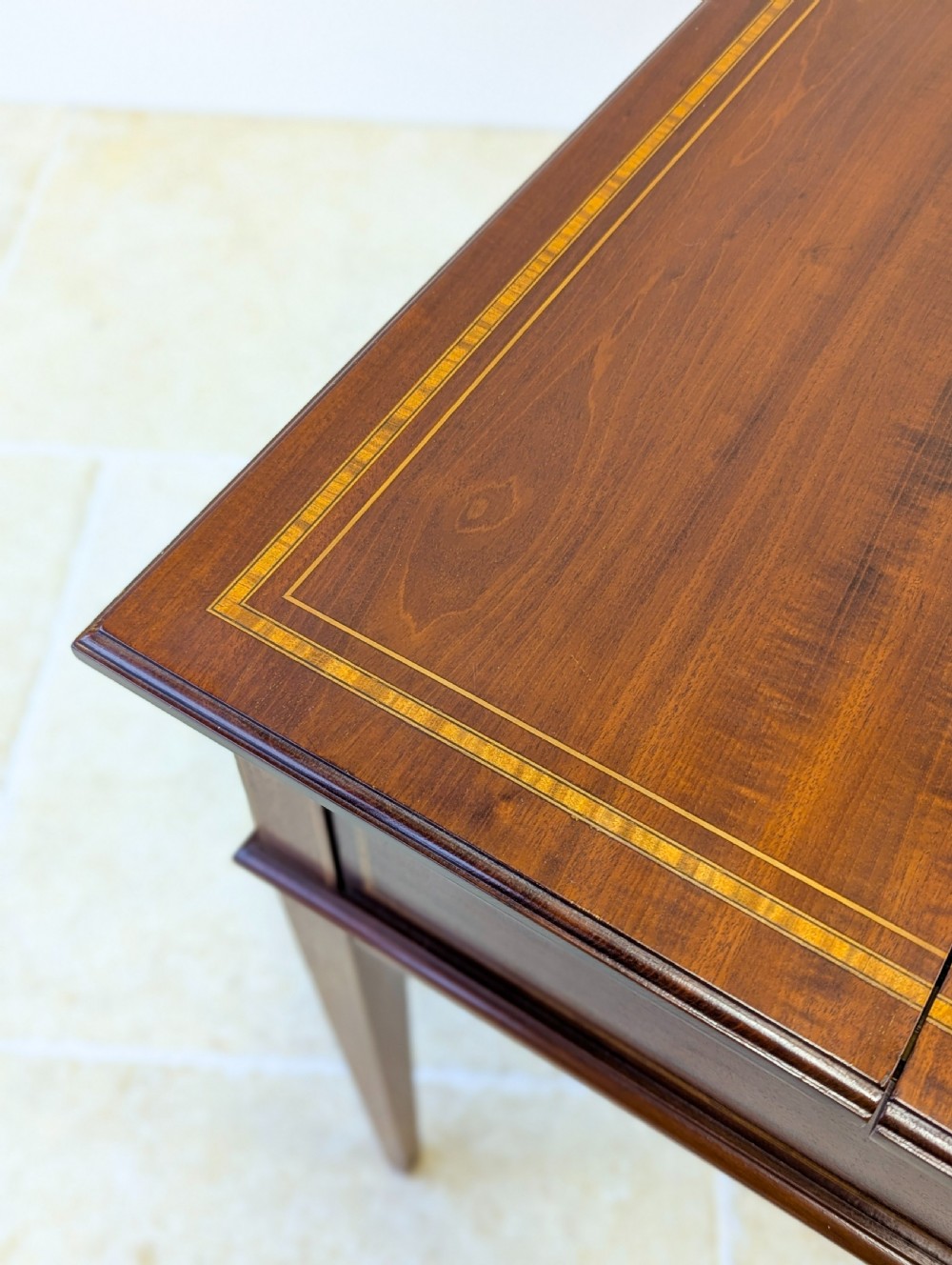 An Edwardian dark mahogany metamorphic writing table featuring two hinged side flaps, a sloped leather writing surface, integrated stationery dividers, and tapered legs. View XIV