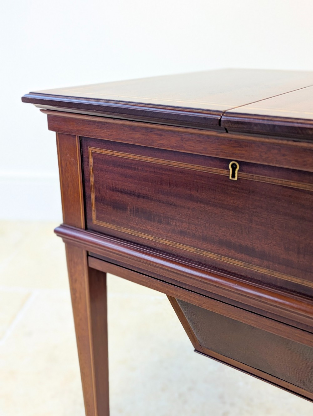 An Edwardian dark mahogany metamorphic writing table featuring two hinged side flaps, a sloped leather writing surface, integrated stationery dividers, and tapered legs. View XVI