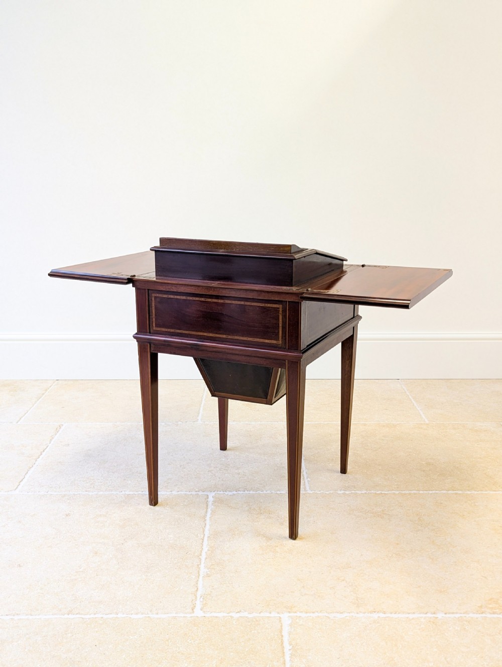An Edwardian dark mahogany metamorphic writing table featuring two hinged side flaps, a sloped leather writing surface, integrated stationery dividers, and tapered legs. View XVII