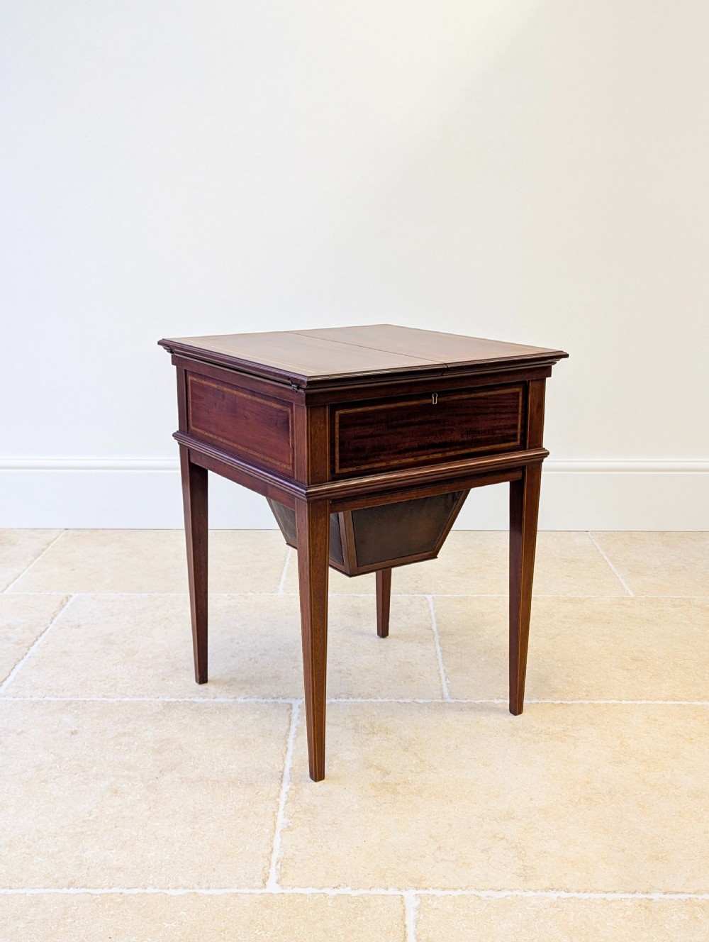 An Edwardian dark mahogany metamorphic writing table featuring two hinged side flaps, a sloped leather writing surface, integrated stationery dividers, and tapered legs. View XVIII