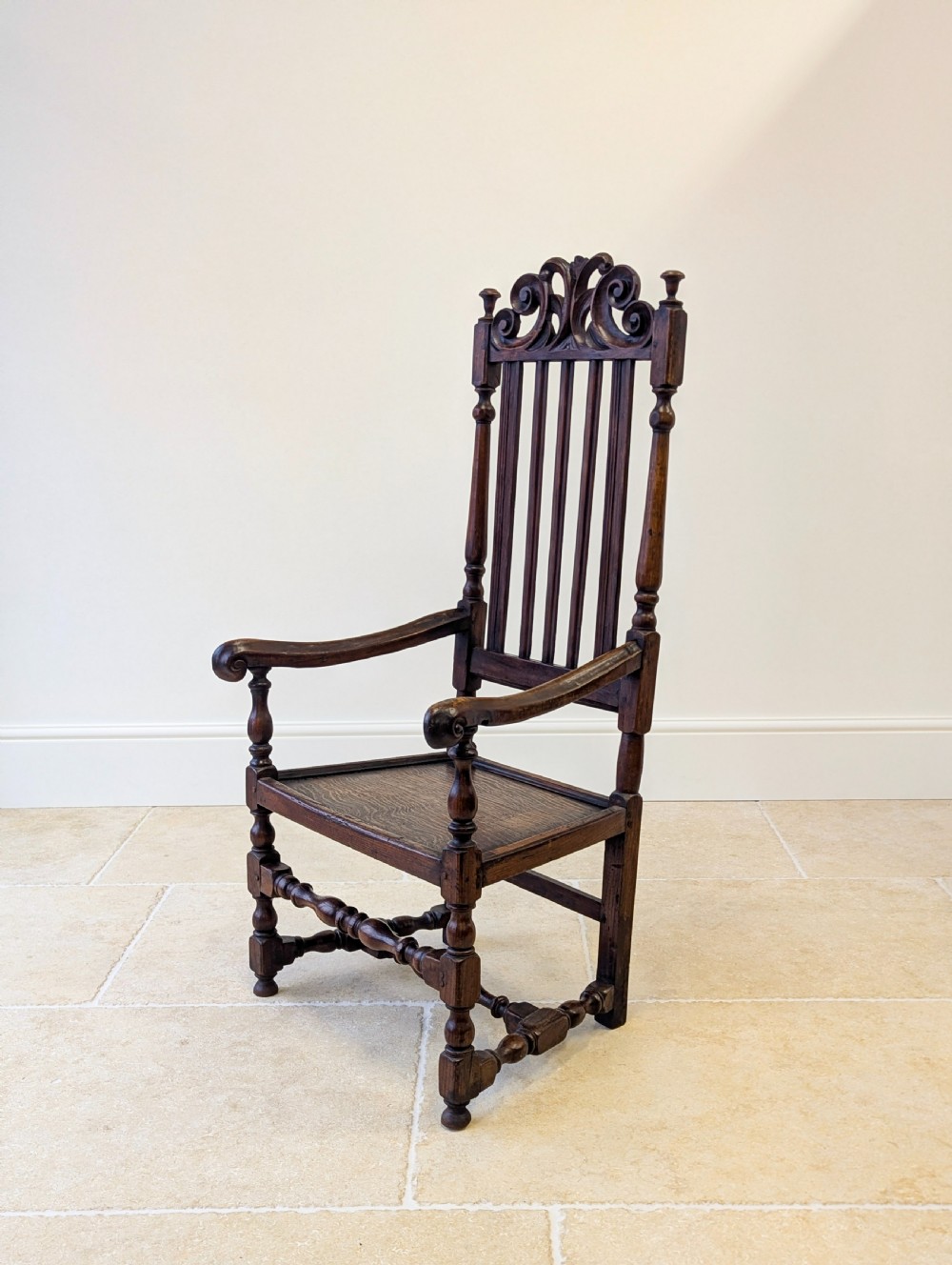 A dark oak William and Mary armchair featuring a carved scrollwork cresting rail, vertical back splats, open arms, and turned legs with stretchers. View VIII