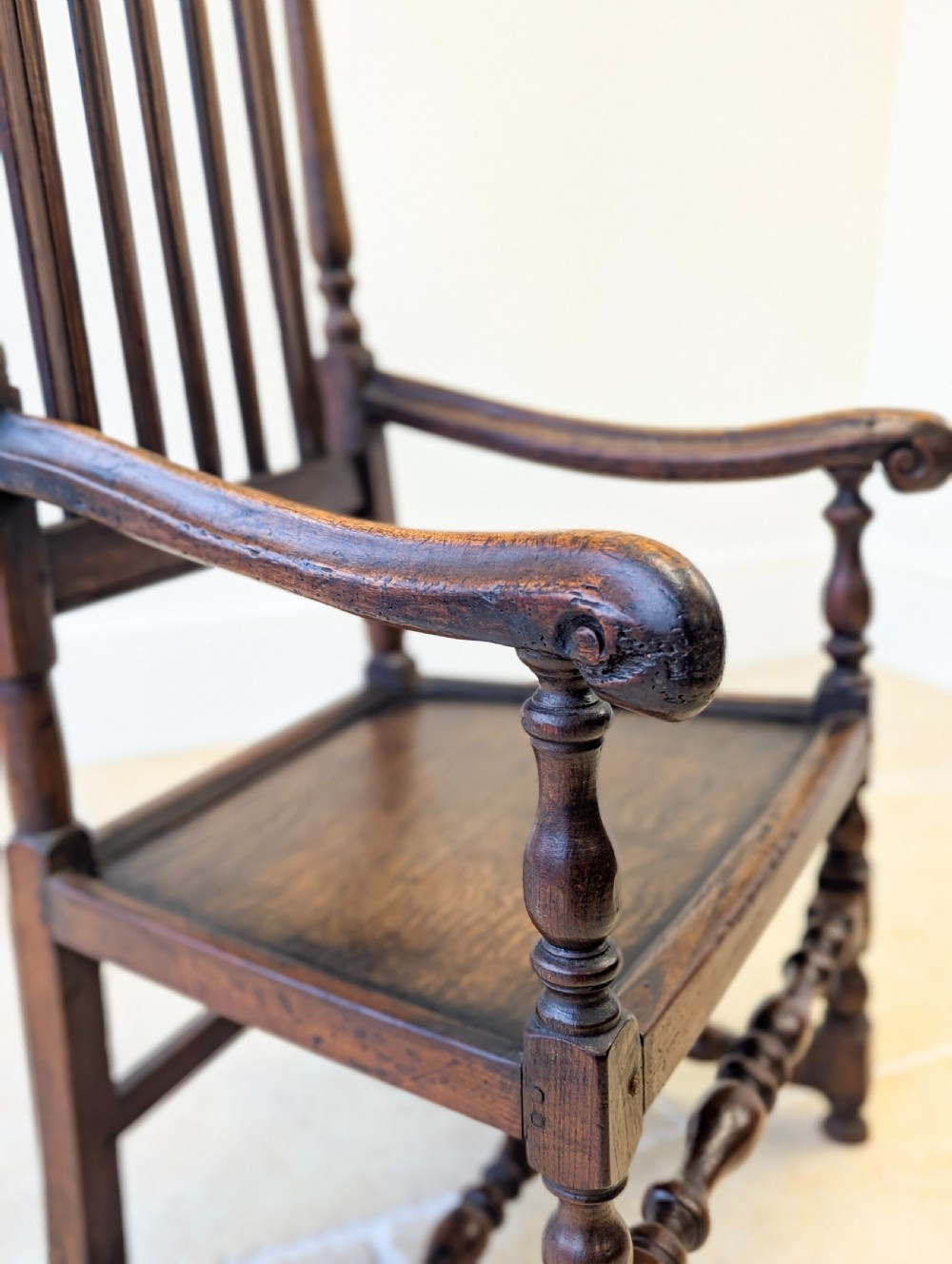 A dark oak William and Mary armchair featuring a carved scrollwork cresting rail, vertical back splats, open arms, and turned legs with stretchers. View XIII