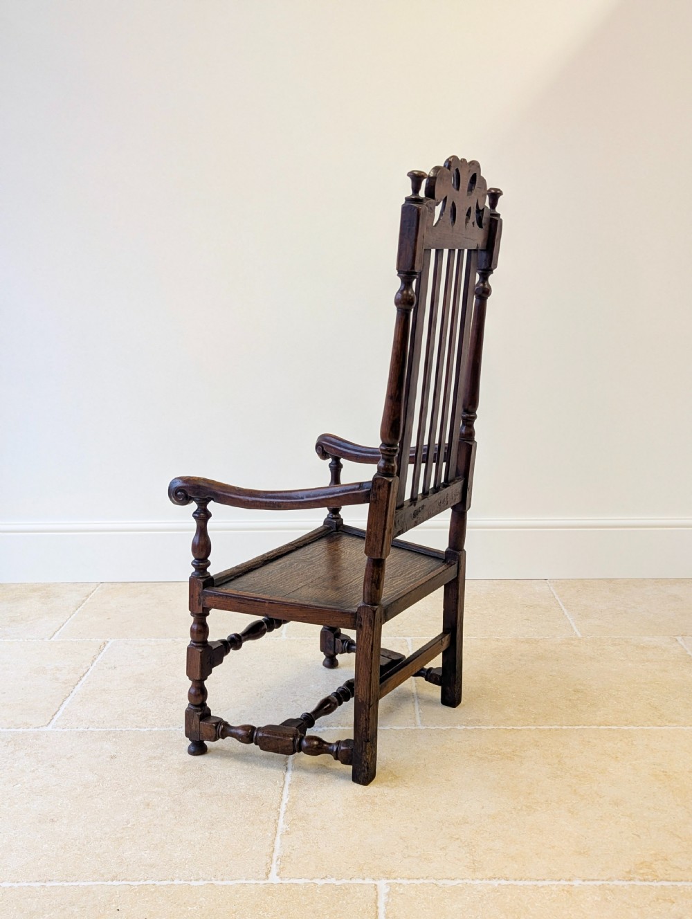 A dark oak William and Mary armchair featuring a carved scrollwork cresting rail, vertical back splats, open arms, and turned legs with stretchers. View XIV