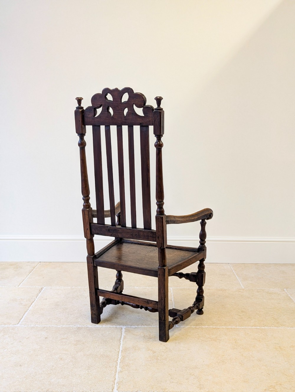 A dark oak William and Mary armchair featuring a carved scrollwork cresting rail, vertical back splats, open arms, and turned legs with stretchers. View XV