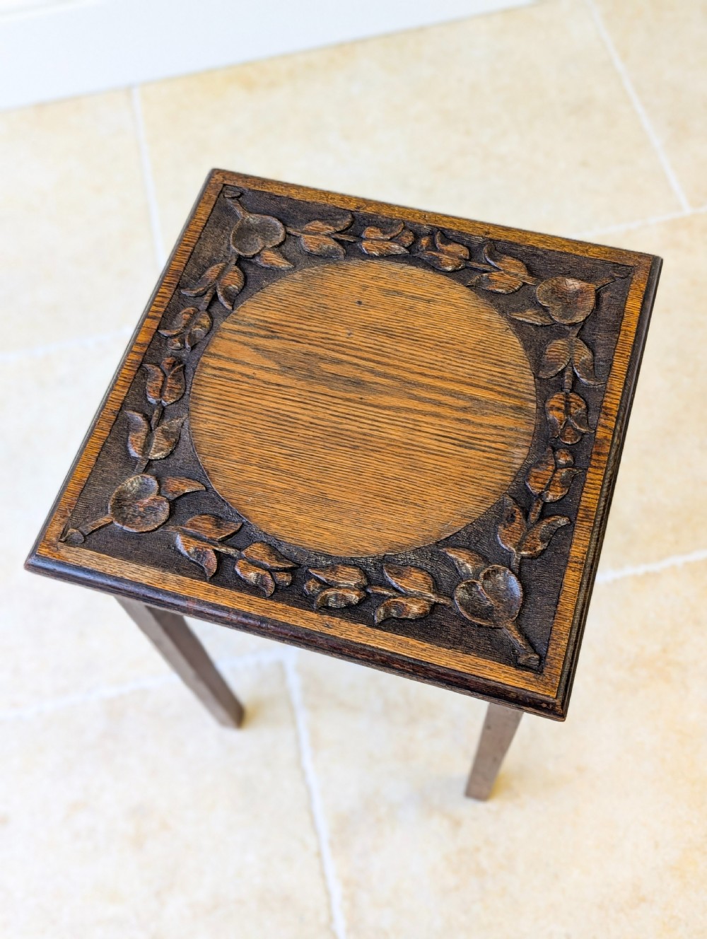 A square dark oak occasional table featuring a relief-carved floral border around a central circular panel, supported by four straight square legs. View II