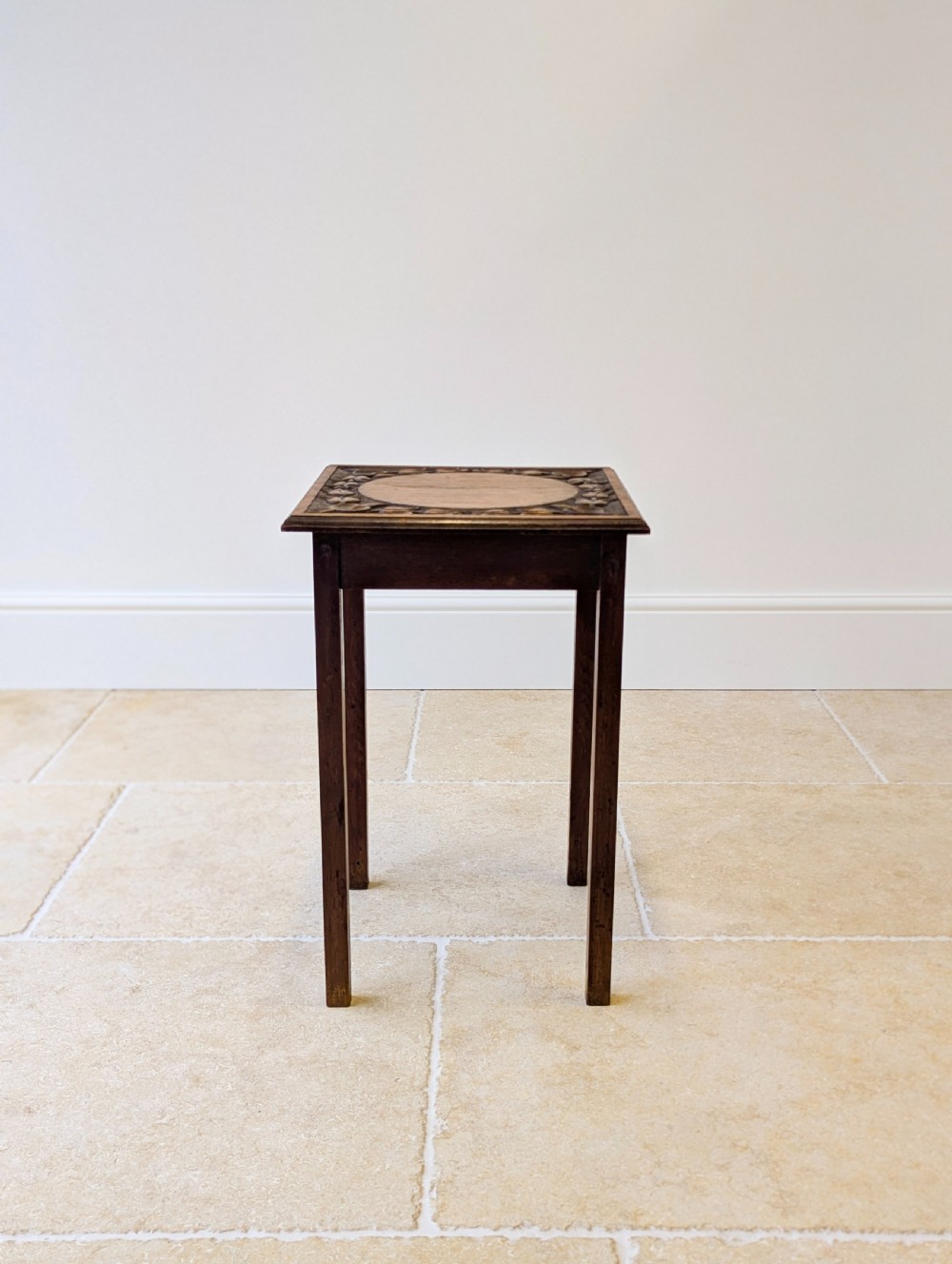 A square dark oak occasional table featuring a relief-carved floral border around a central circular panel, supported by four straight square legs. View III