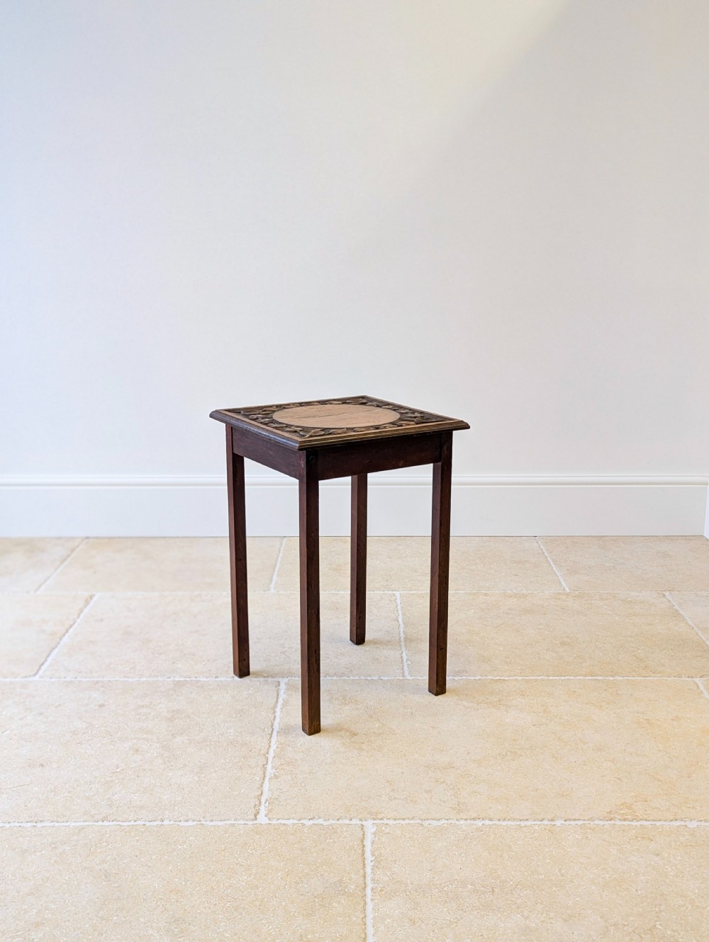 A square dark oak occasional table featuring a relief-carved floral border around a central circular panel, supported by four straight square legs. View VI