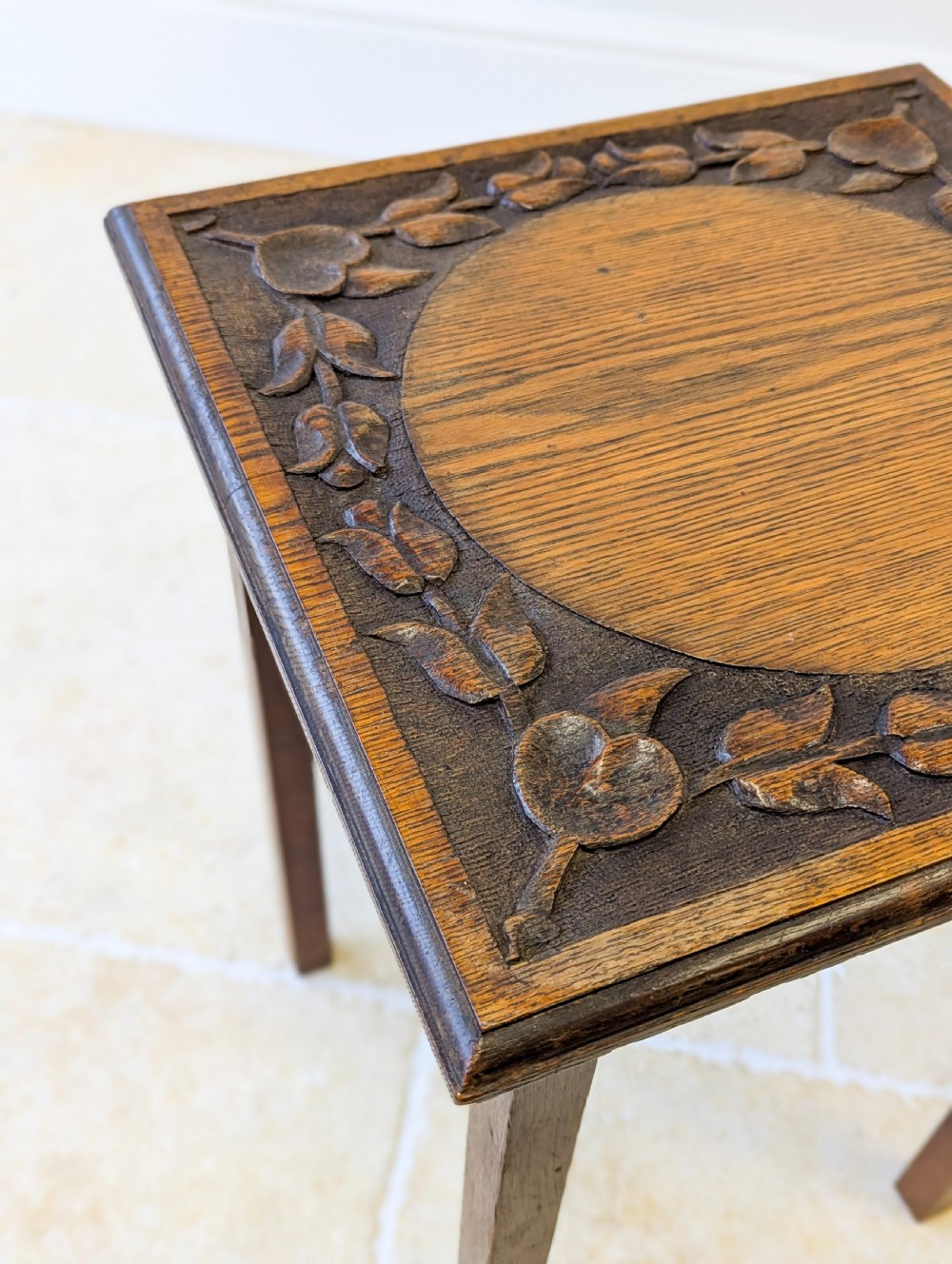 A square dark oak occasional table featuring a relief-carved floral border around a central circular panel, supported by four straight square legs. View VIII