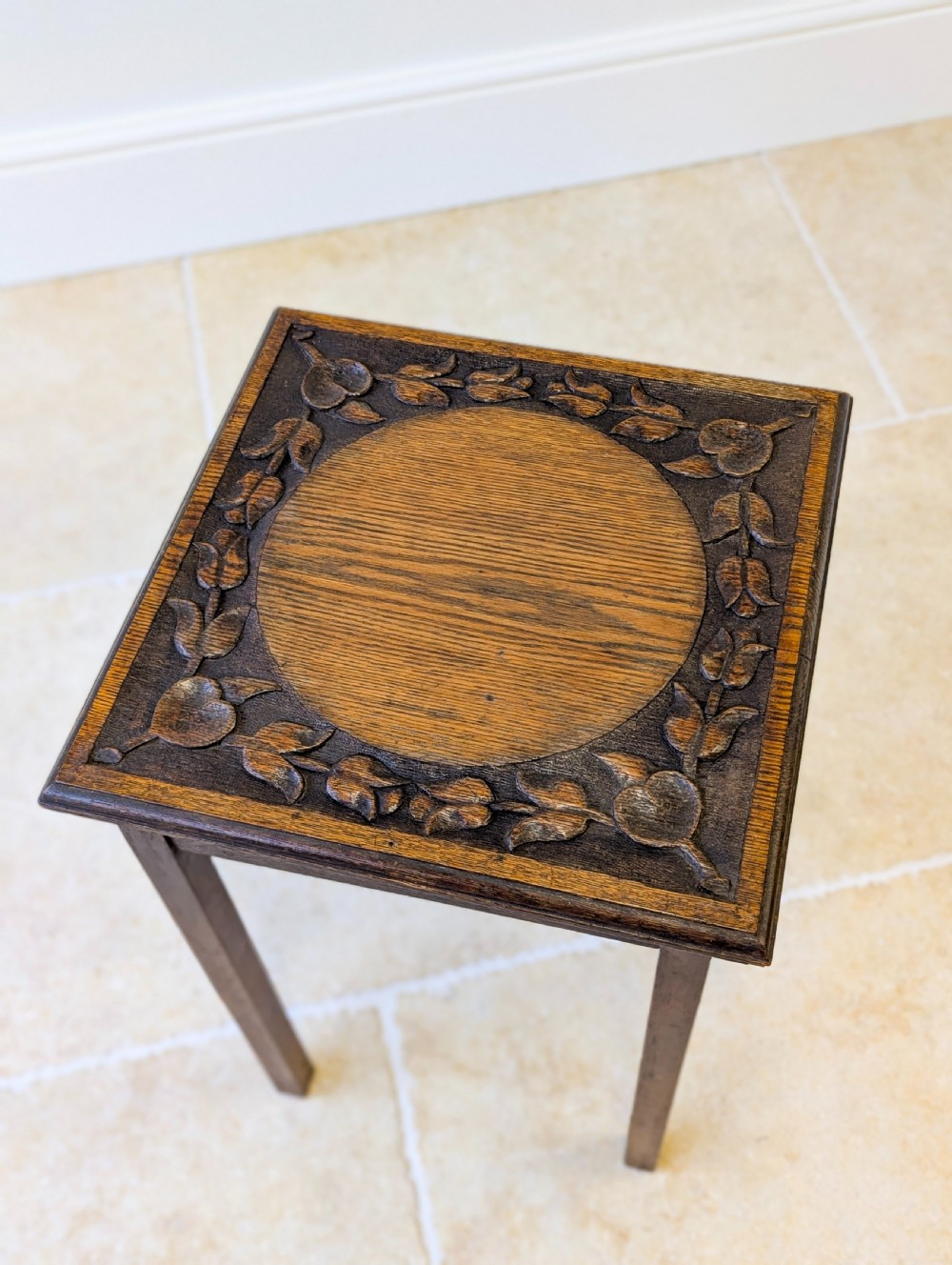 A square dark oak occasional table featuring a relief-carved floral border around a central circular panel, supported by four straight square legs. View XI
