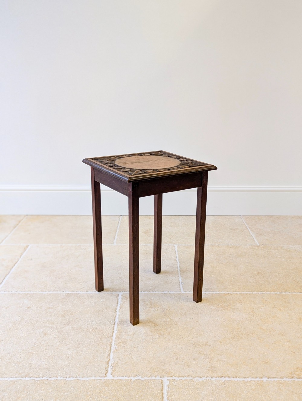 A square dark oak occasional table featuring a relief-carved floral border around a central circular panel, supported by four straight square legs. View XIV