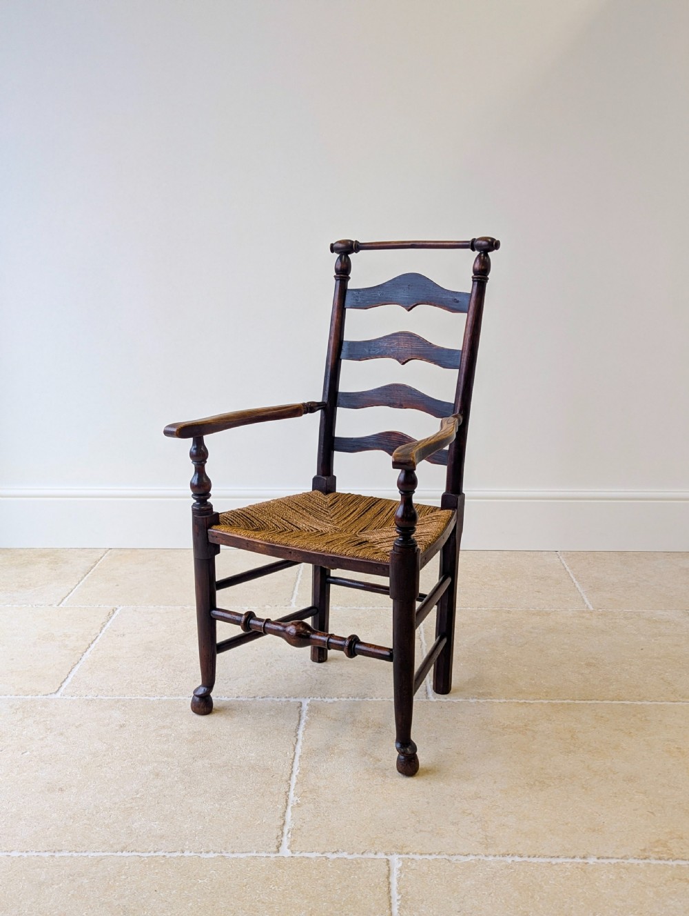 A late nineteenth-century country ash armchair featuring a ladderback design with four curved horizontal slats, turned armrest supports, and a hand-woven natural rush seat.